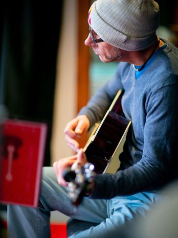 Man wearing a beanie playing an acoustic guitar indoors.