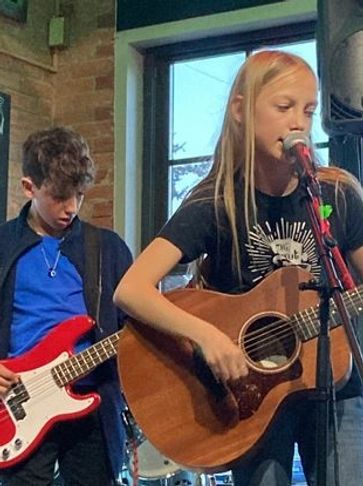 Two young musicians playing guitar and bass during a live indoor performance.