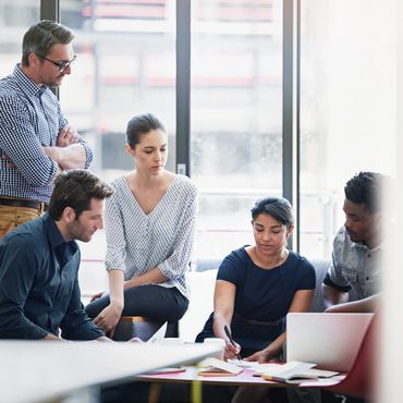 A team engaged in a focused collaborative meeting with documents and a laptop.