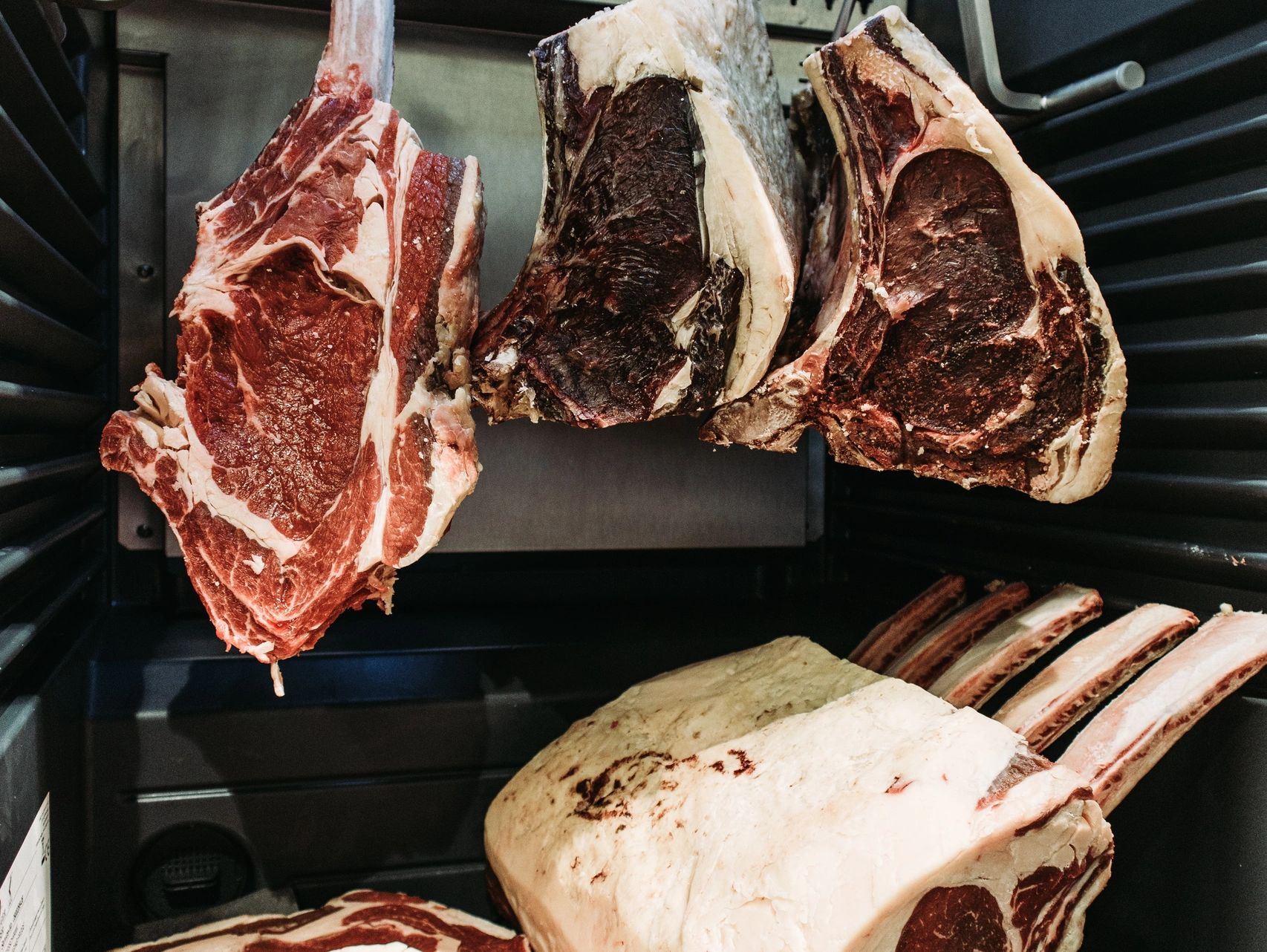 Côtes de viande en maturation suspendues dans une chambre froide.