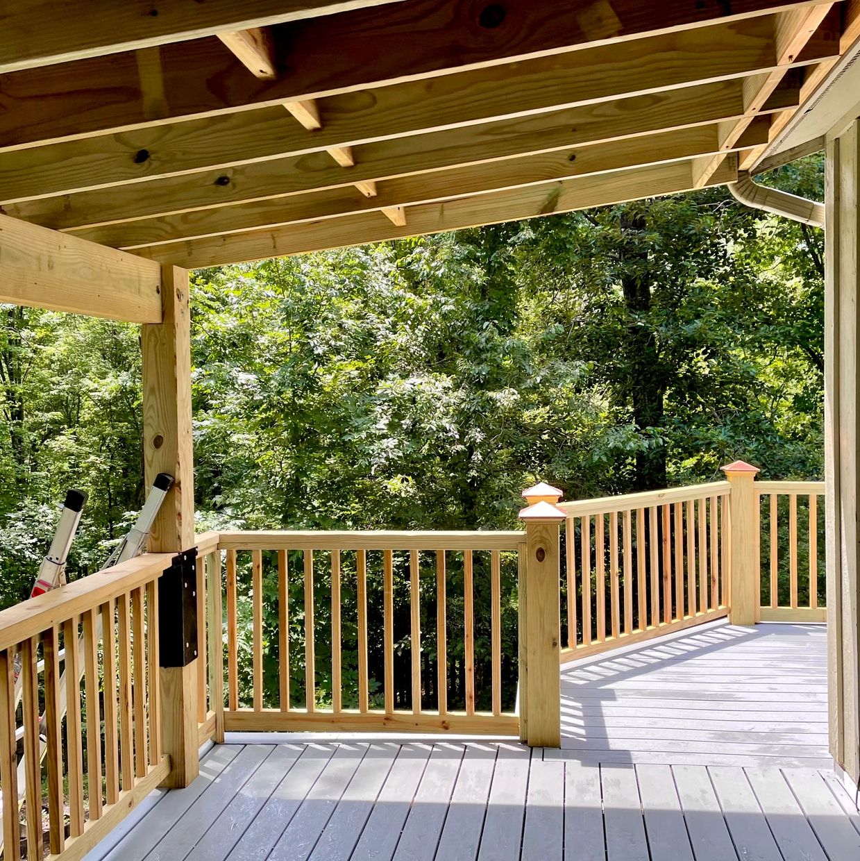 Newly built wooden porch with railings surrounded by green trees.