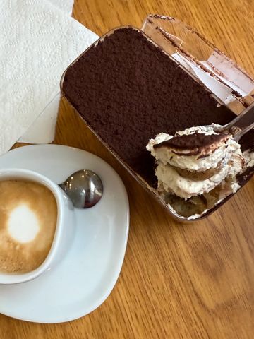 Cup of coffee with a creamy dessert topped with cocoa powder on a wooden table.