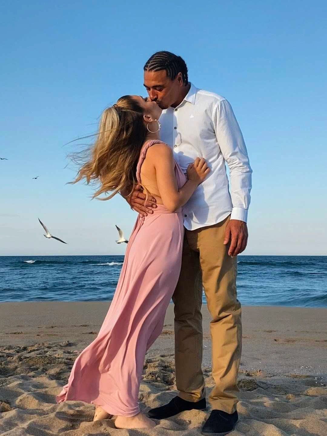 Couple kissing on a beach with seagulls flying in the background.