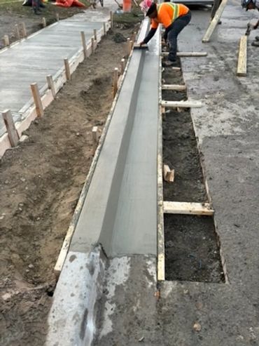 Construction worker smoothing freshly poured concrete curb on a street.