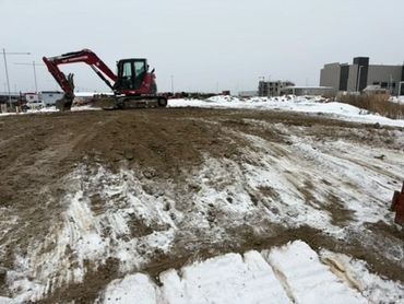 Excavator working on muddy, snowy construction site in winter.