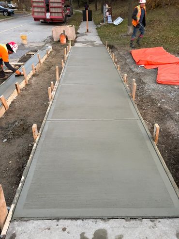 Freshly poured concrete sidewalk with workers smoothing the edges.