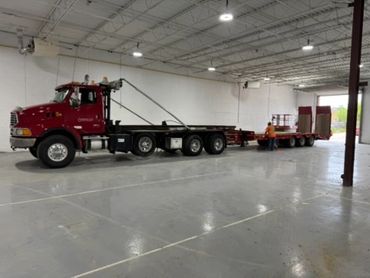 A red flatbed truck inside a spacious warehouse with a worker nearby.