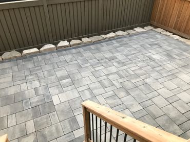 A newly paved patio with gray stone tiles and wooden fence.