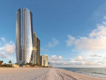 Tall modern building by the beach under a blue sky.