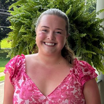 Smiling woman in a pink floral top with a green fern behind her.