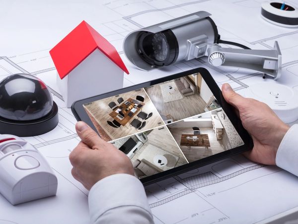 A Person Watching Footage On Digital Tablet With Security Equipments And House Model On Blueprint