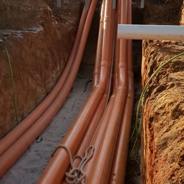 Orange conduit pipes laid in a trench at a work site.