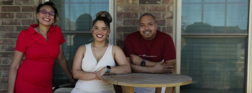 Three people smiling around a wooden table on a porch.