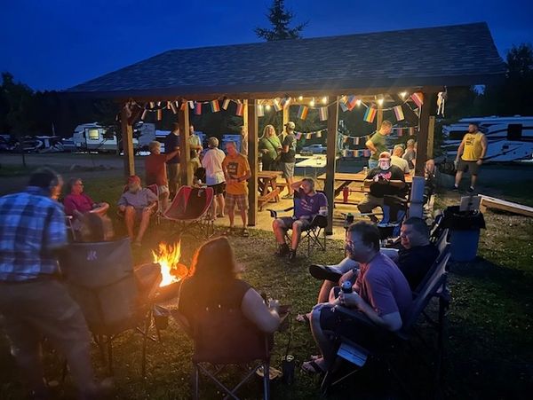 People gathered around a campfire and pavilion at night with festive lights and flags.