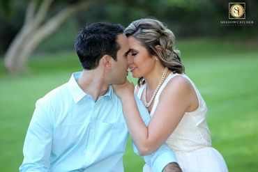 Natural, romantic photo of a couple sitting in the park. She is wearing a white dress and pearls.