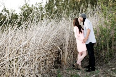 Candid photo of a couple in a sweet embrace kissing in a field of tall dry reeds.