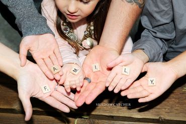 Fun family photo of the families hands together, holding scrabble tiles that spell FAMILY