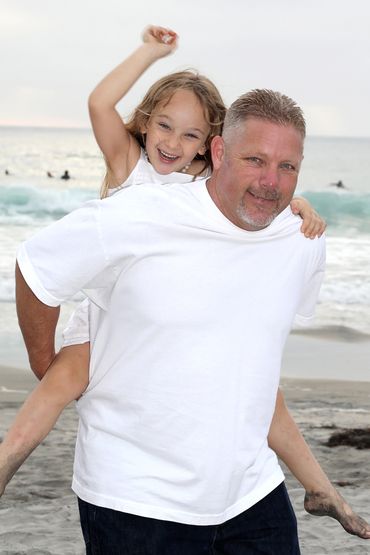 Dad on the beach with his daughter getting a piggyback ride.