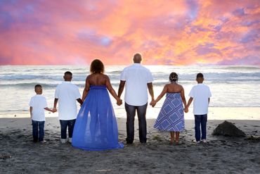 Family portrait of a family at the beach at sunset holding hands facing away watching a colorful sun