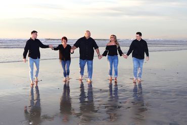 Family portrait of five, holding hands walking in the ocean, they are reflected in the water.