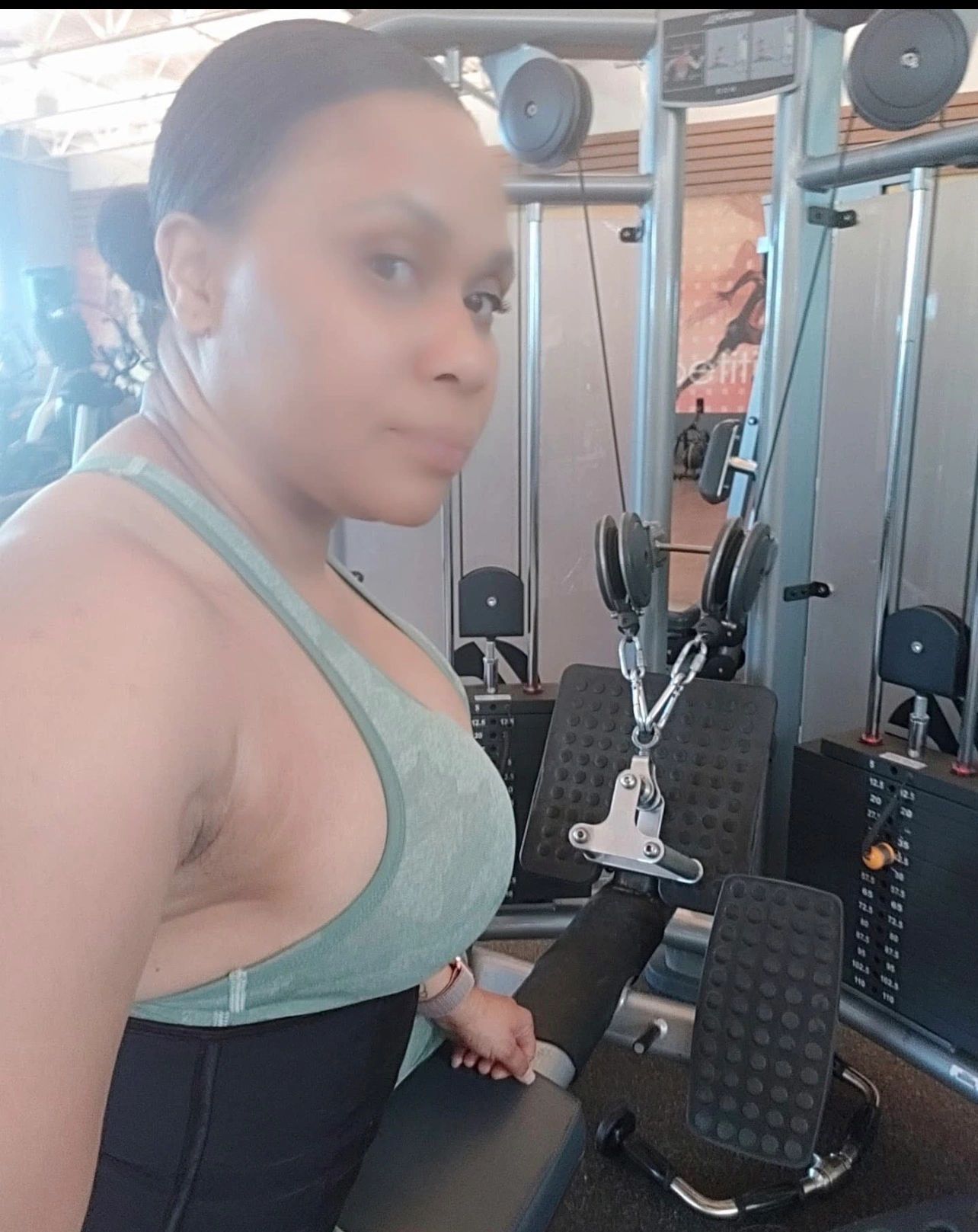 Woman in gym gear posing next to exercise machine.
