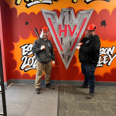 Two men in safety gear stand with bats in front of a colorful Wreck Room wall.