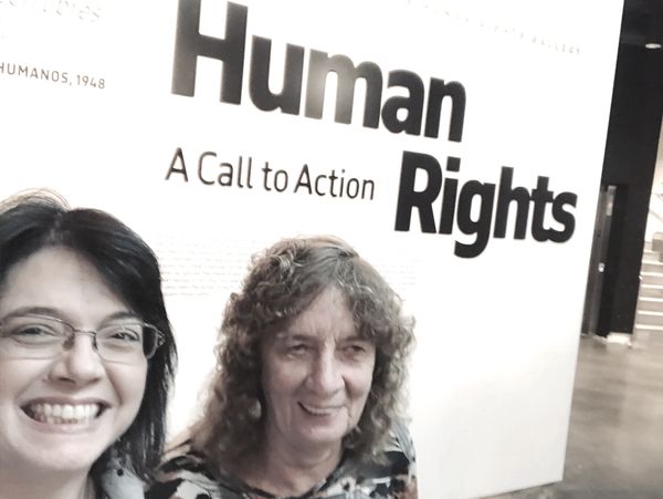 Two smiling women stand in front of  a wall with words that read "Human Rights; a call to action."