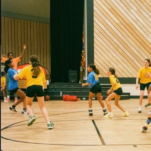 Girls playing basketball indoors in yellow and blue jerseys.
