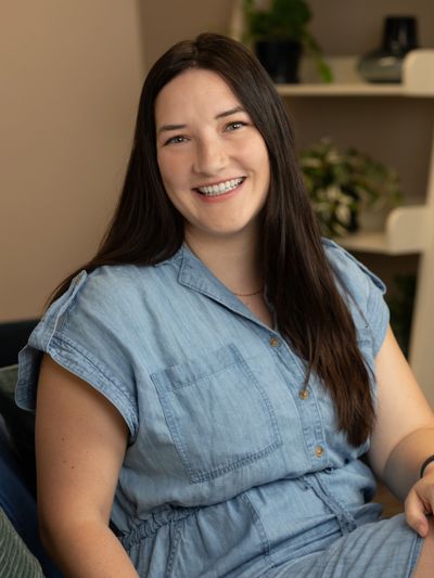 Smiling woman in a blue denim dress sitting indoors.