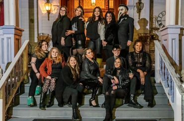 Group of women and one person in a plague doctor mask posing on steps.