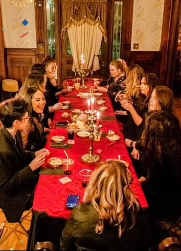 A group of people enjoying a candlelit dinner around a red tablecloth-covered table.