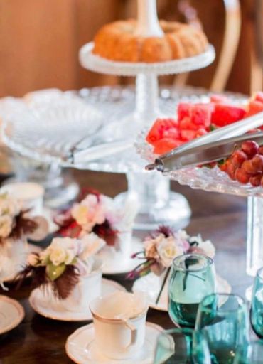 Elegant table setting with floral decor, tea cups, and a tiered tray of fruits and cake.