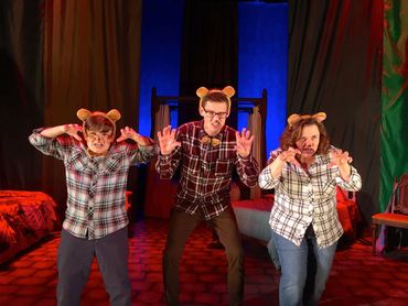 Three people in bear ears and plaid shirts acting fierce on stage.