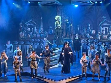 A large group of actors performing a theatrical play with spooky costumes and graveyard backdrop.