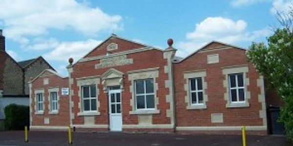 A small, old red brick building with white window frames under a blue sky.