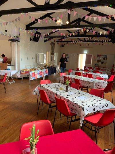 Community hall decorated with bunting, red chairs, and tables set for an event with food buffet.