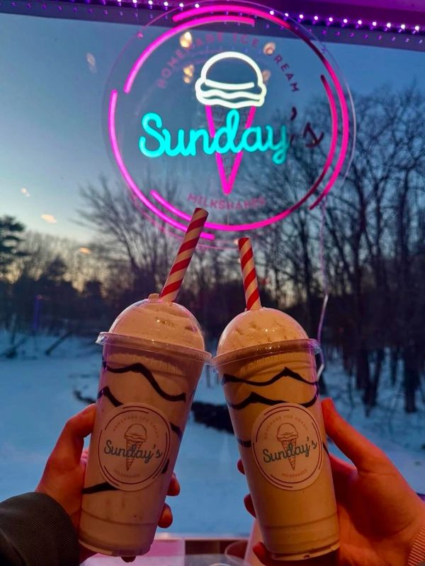 Two milkshakes from Sunday's held up against a snowy window.