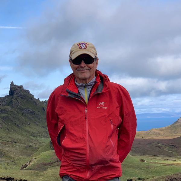 Man in red jacket and cap standing in a scenic mountainous landscape.