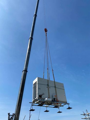 Crane lifting a large industrial HVAC unit against a clear blue sky.