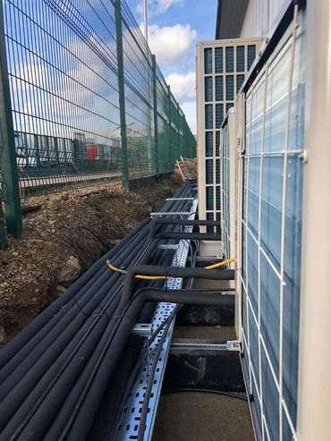 Outdoor air conditioning units with insulated pipes along a fenced area.
