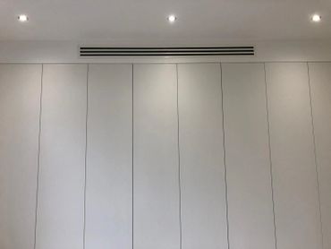 Minimalist white wall with vertical panels and recessed ceiling lights.