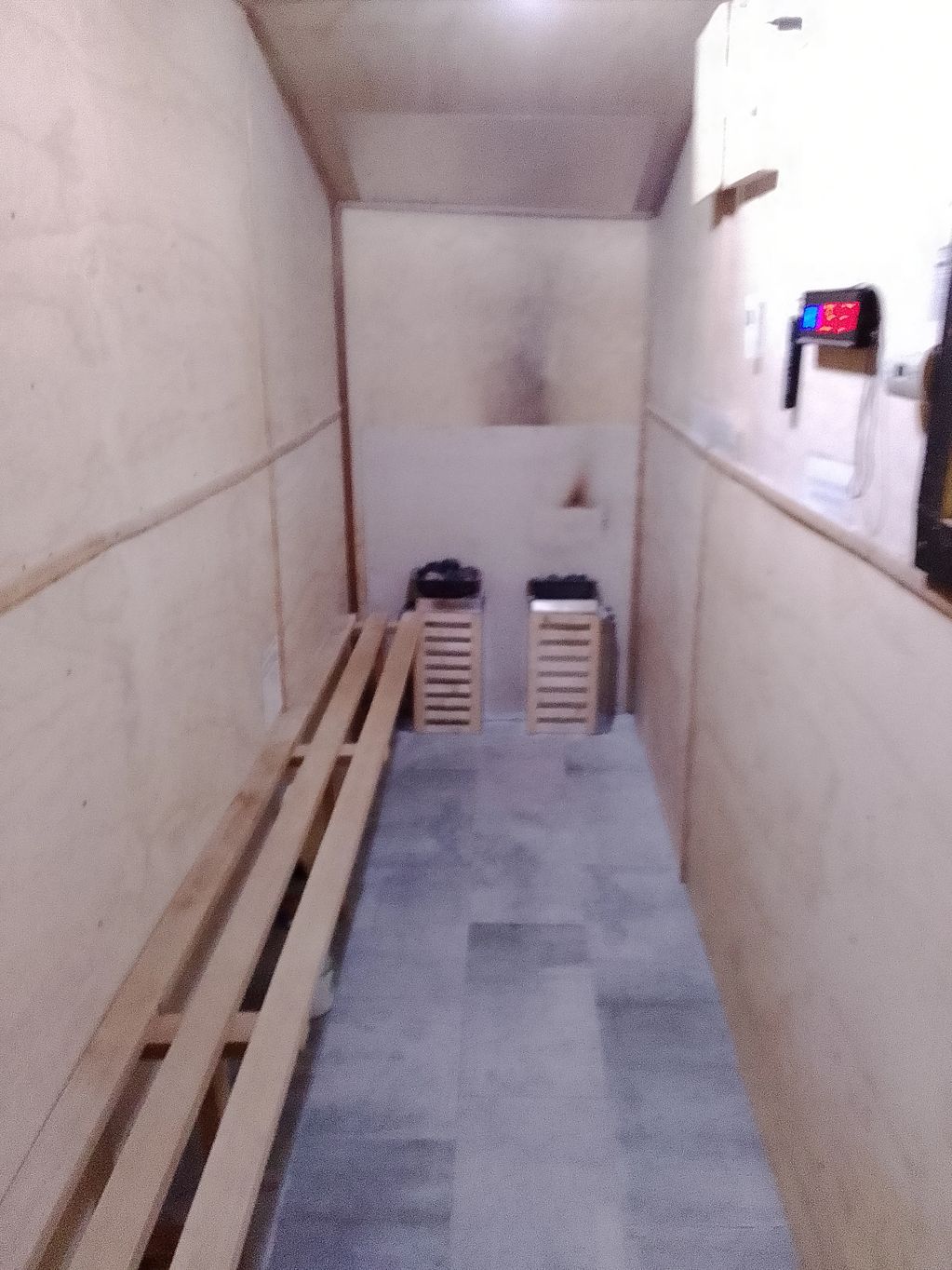 Narrow room with wooden bench and two heaters at the end.