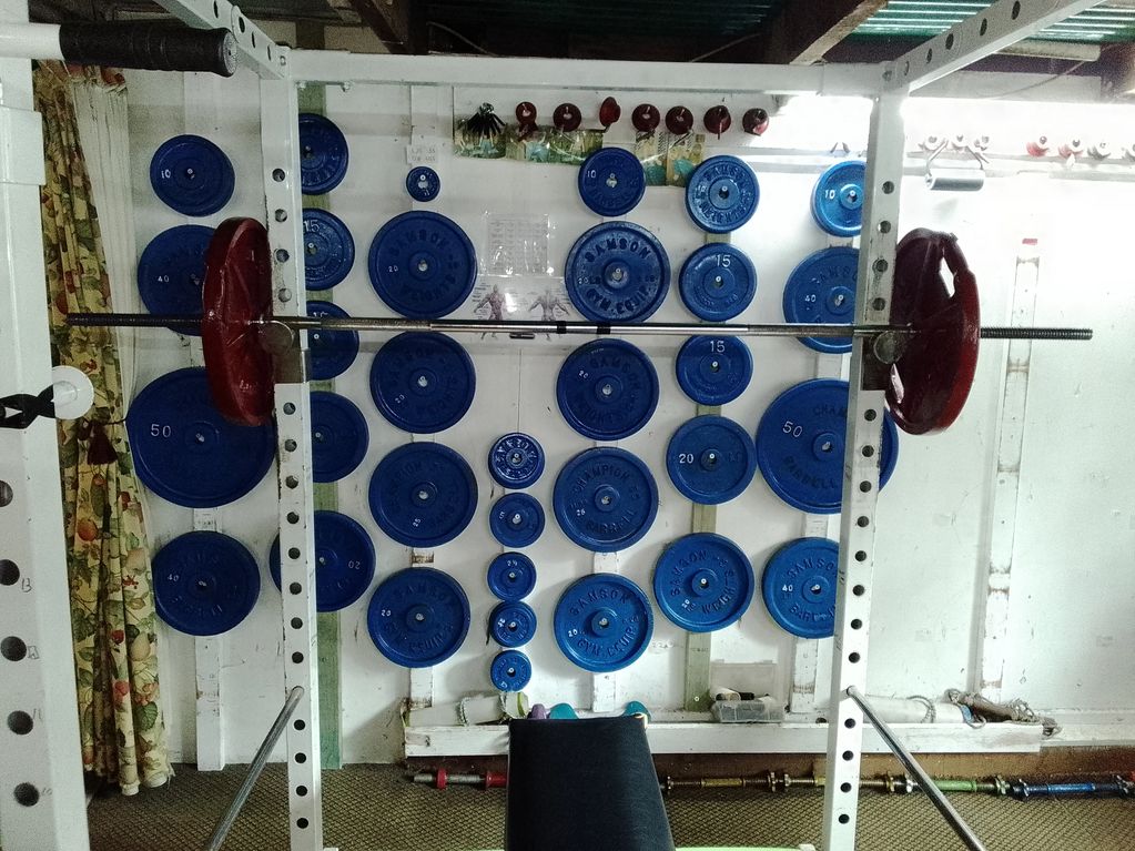 A home gym setup with a barbell and weight plates neatly arranged on the wall.