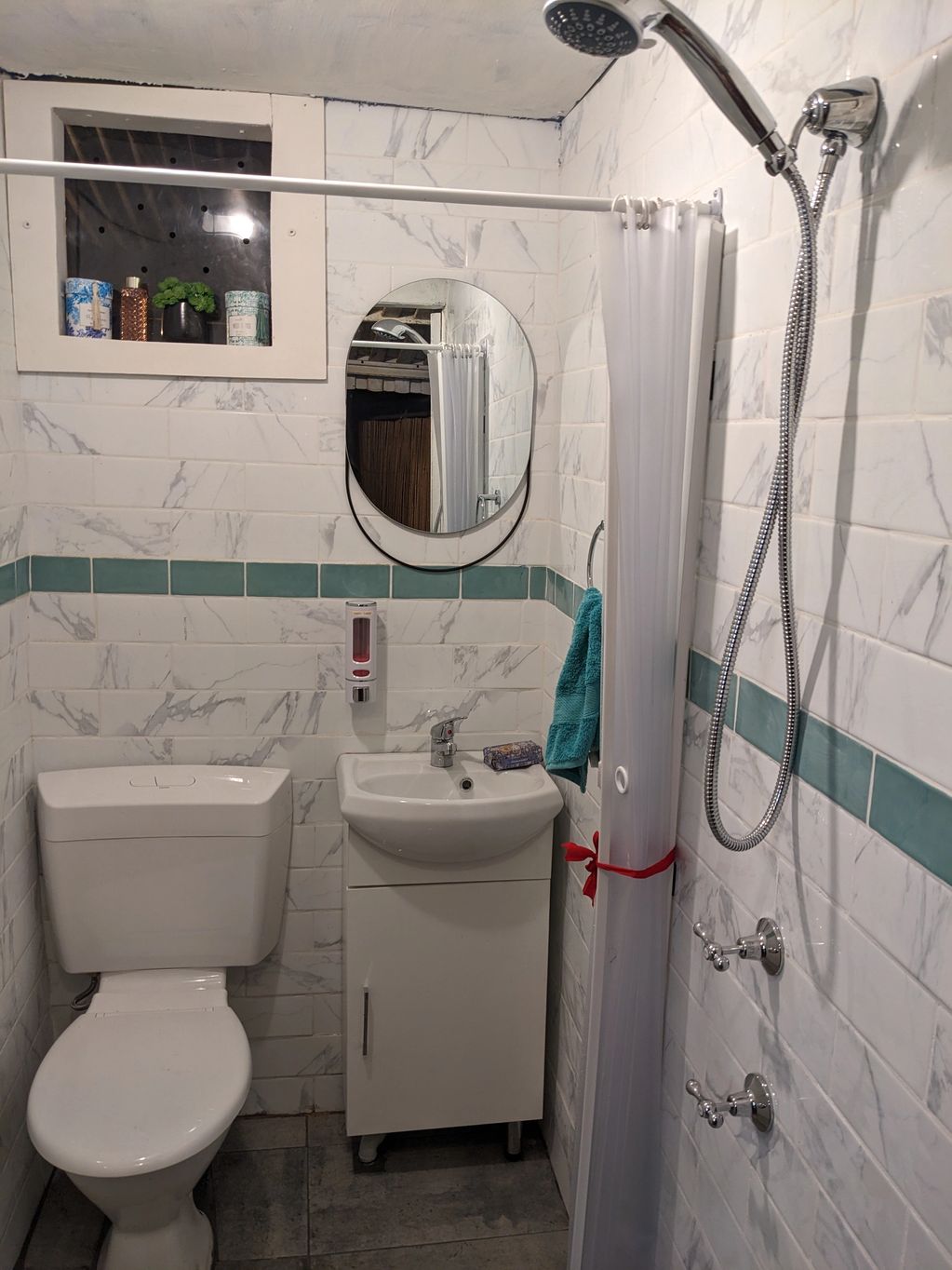 Compact bathroom with white fixtures and teal accents in tiles and towel.