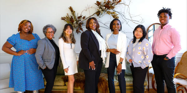 Diverse group of seven professionals posing indoors, smiling confidently.