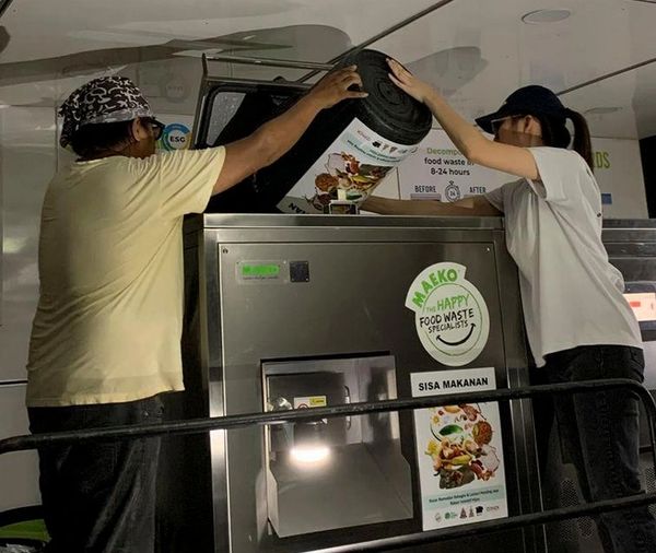 Two people disposing food waste into a machine.