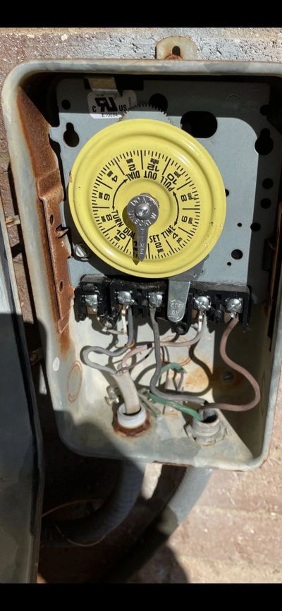 Old mechanical timer switch inside a metal box with wires and rust.