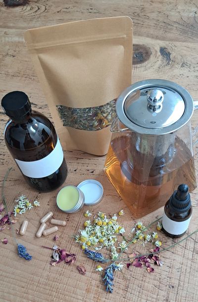 Natural herbal remedies with dried flowers, tincture, capsules, and a glass teapot.