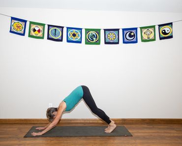 Woman practicing yoga in downward dog pose under religious symbol flags.