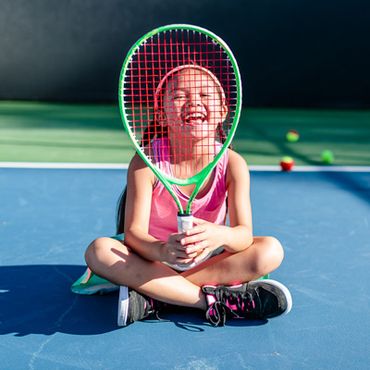 little girl smiling with racquet on tennis court